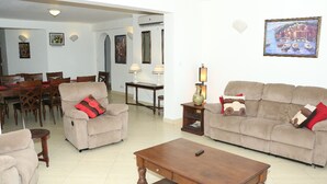 A living room with two sofas, a coffee table, and a dining area with chairs and a table. - Wild Flower Apartment (Mombasa)