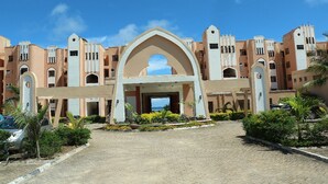 A hotel entrance with a central archway, multiple balconies, and a paved driveway. - Wild Flower Apartment (Mombasa)