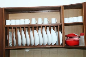A kitchen cabinet with white mugs, plates, and bowls.