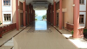 A corridor with a view of the sea, featuring a tiled floor and red pillars. - Wild Flower Apartment (Mombasa)
