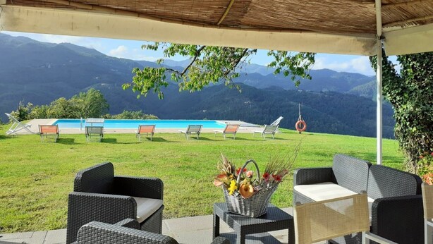 Ein überdachter Außenbereich mit Korbmöbeln, einem Pool und Blick auf die Berge.