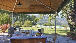 Ein Essbereich im Freien mit Tisch und Geschirr, umgeben von Stühlen, unter einem Reetdach.