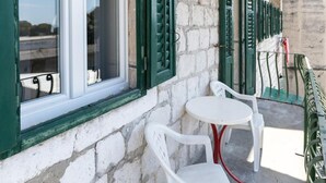 Ein Steinhaus mit grünen Fensterläden, weißen Fensterrahmen und Außenbereich mit weißen Plastikstühlen und einem kleinen runden Tisch.