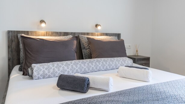 Ein ordentlich bezogenes Bett mit gemusterten Kissen, einem Kopfteil und zwei Nachttischlampen.