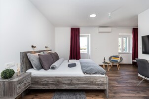 Quarto moderno com cama de madeira, mesinha de cabeceira pequena, tapete cinza e TV na parede.
