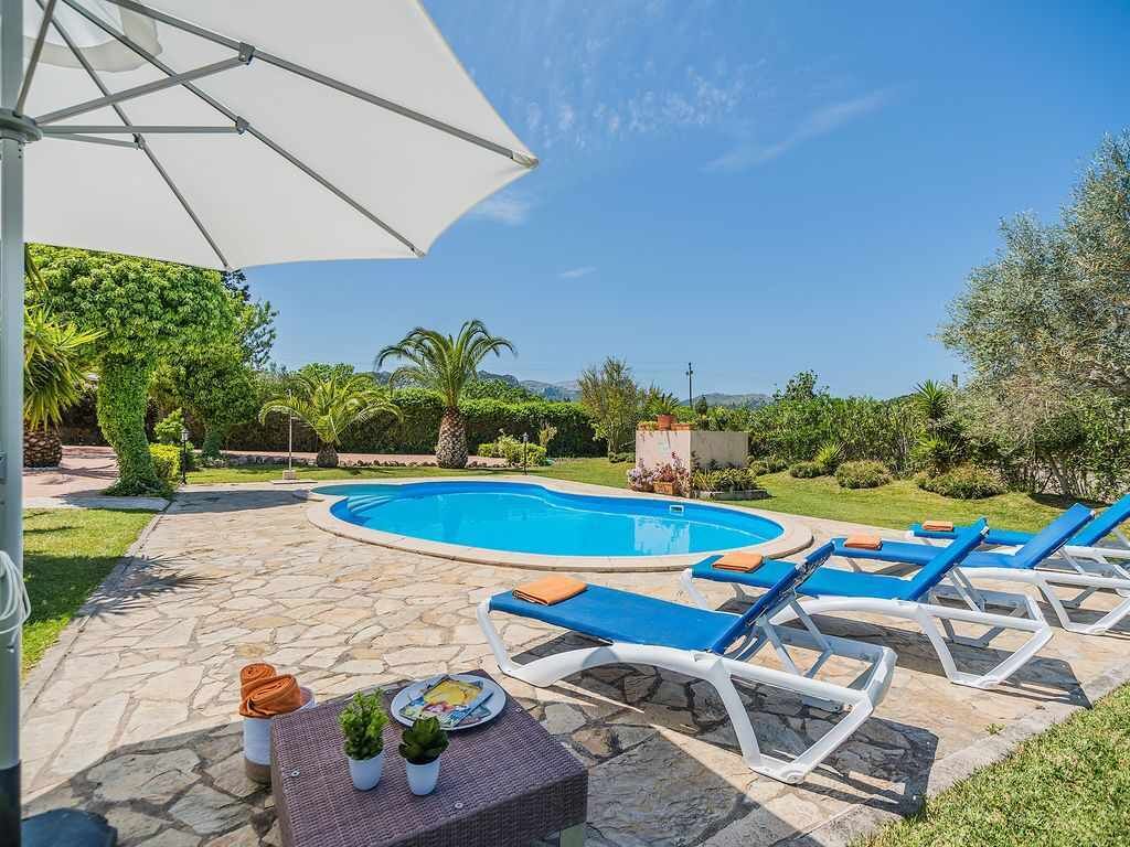 A swimming pool with lounge chairs and a table with plants, surrounded by a stone patio and greenery.