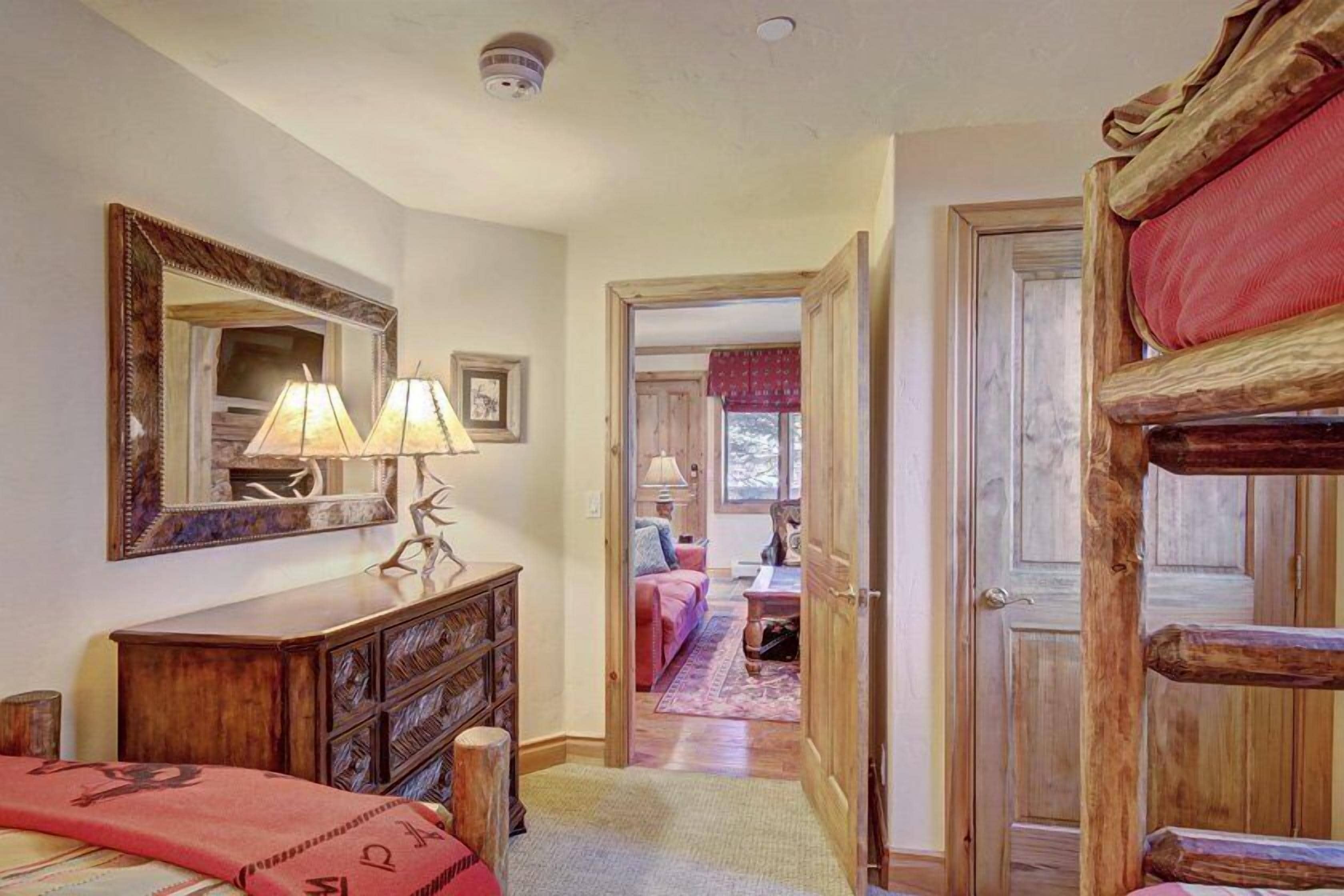 A cozy room with a wooden dresser, a mirror, and a bed with a red blanket.