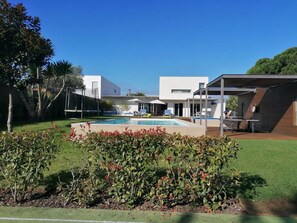 A modern outdoor pool area with a clear blue sky, surrounded by well-maintained grass and shrubs.