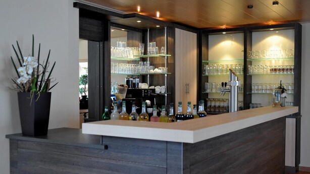 A bar area with a counter, shelves with glasses and bottles, and a potted plant. - Landhotel Buchenkrug (Halle Westphalia)