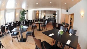 A spacious dining area with multiple tables and chairs, a large plant, and a curved ceiling. - Landhotel Buchenkrug (Halle Westphalia)