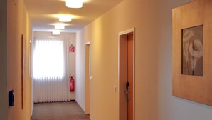 A hallway with a wooden door, a framed picture on the wall, and a fire extinguisher near the window. - Landhotel Buchenkrug (Halle Westphalia)