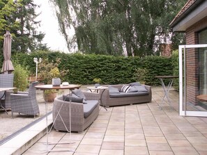 An outdoor patio area with wicker furniture, including sofas and chairs, a round table, and a small table with a lamp. - Landhotel Buchenkrug (Halle Westphalia)