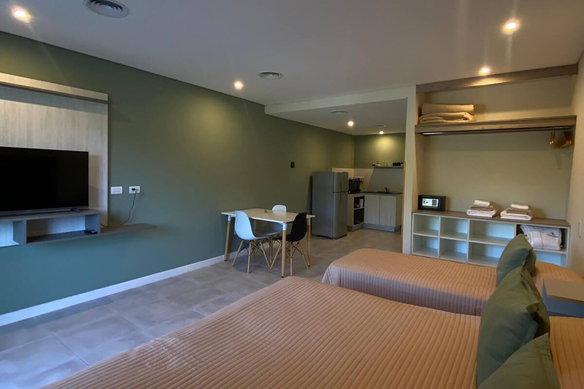 Ein Hotelzimmer mit zwei Betten, einem Fernseher, einem Schreibtisch und einer Küchenzeile.