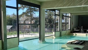 An indoor swimming pool with large windows, a lounge area, and a view of the outside. - Los Robles Apart Hotel (Sierra de la Ventana)