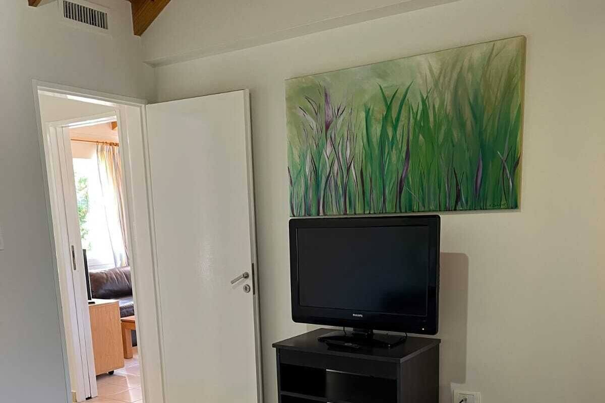 Ein Schlafzimmer mit einem Bett, einem Fernseher auf einem Schrank, einem Bild an der Wand und einer Tür zu einem anderen Raum.