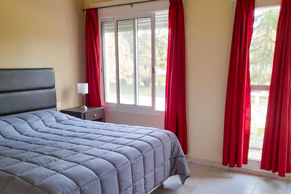 Ein Schlafzimmer mit einem großen Bett, einem Nachttisch, einem Fenster mit roten Vorhängen und Blick ins Freie.
