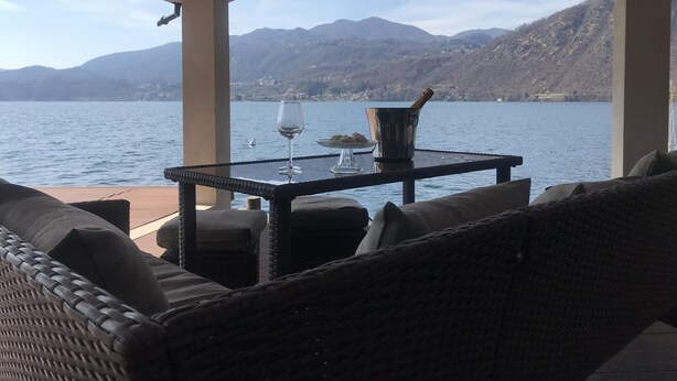 A covered outdoor seating area with a table, a glass of wine, and a champagne bucket. - LA PLAYA: Villa with a Private Beach and All-Inclusive Sports  (Pettenasco)