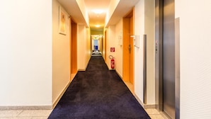 Un pasillo de hotel con piso alfombrado, puertas de madera y un ascensor a la derecha.