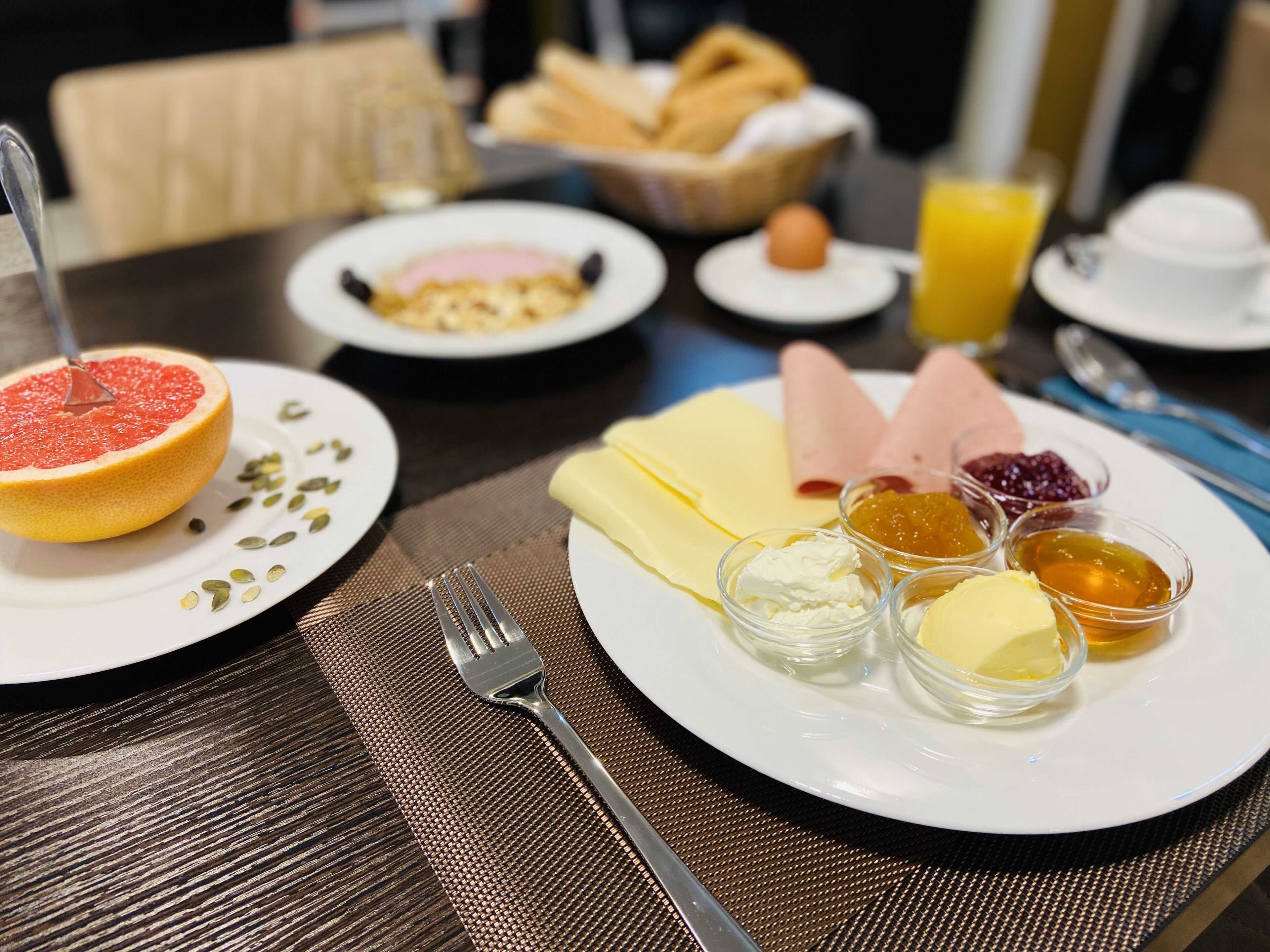 A breakfast setting with a plate of food including a grapefruit, cheese, ham, and condiments.
