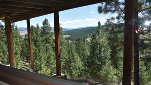 Un balcon en bois offrant une vue sur une forêt dense et des montagnes lointaines.
