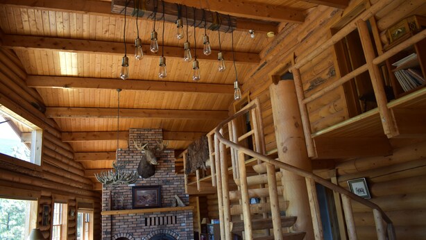 L’intérieur d’une cabane en rondins, avec une cheminée en briques, des poutres en bois et un escalier en colimaçon.