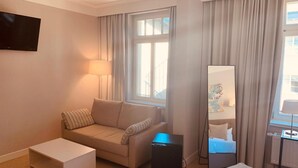 Ein Hotelzimmer mit einer Couch, einem kleinen Tisch, einem Fernseher, einem Spiegel und einem Bett.