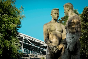 Una estatua de dos figuras en un parque, con una estructura moderna al fondo.