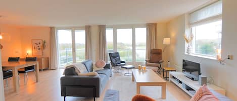 A modern living room with a sofa, armchair, coffee table, TV, and dining area.