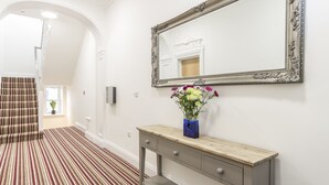 En hall med ett randigt golv, ett träbord med en vas med blommor och en stor, utsmyckad spegel på väggen.