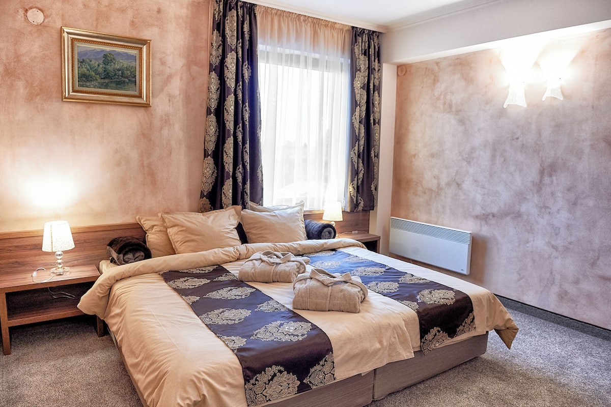 A neatly made bed with a floral bedspread, a nightstand with a lamp, and a painting on the wall.