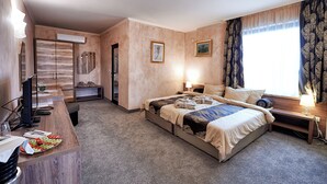 A hotel room with a bed, bedside table, lamp, and a desk with a computer and a fruit bowl. - Platinum Image Hotel (Elin Pelin)