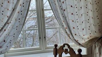 A room with a wooden chair, a window with white curtains, and a view of trees outside.