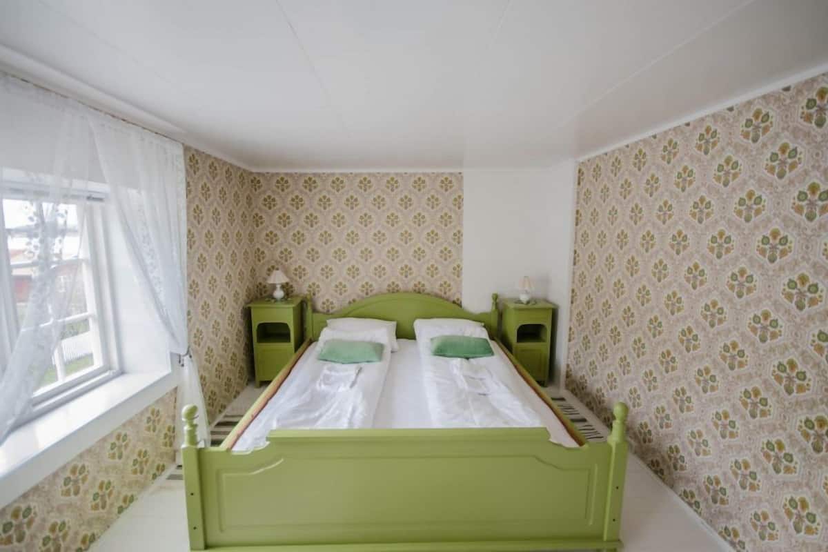 Una habitación con una cama verde, dos mesitas de noche y papel tapiz estampado.
