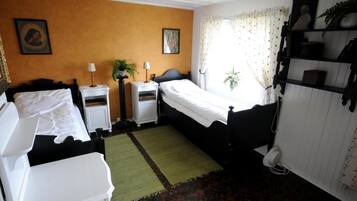 Ein Zimmer mit zwei Betten, einem Nachttisch mit Lampe, einem kleinen Tisch mit Pflanze und einem Heizkörper.