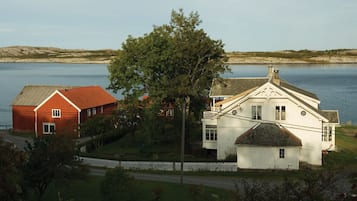 Una casa blanca y roja con un árbol grande frente a ella, a orillas de un lago.