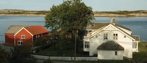 A red and white house with a large tree in front, situated by a lake.