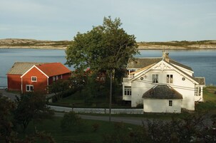 Una casa blanca y roja con un árbol grande frente a ella, a orillas de un lago.