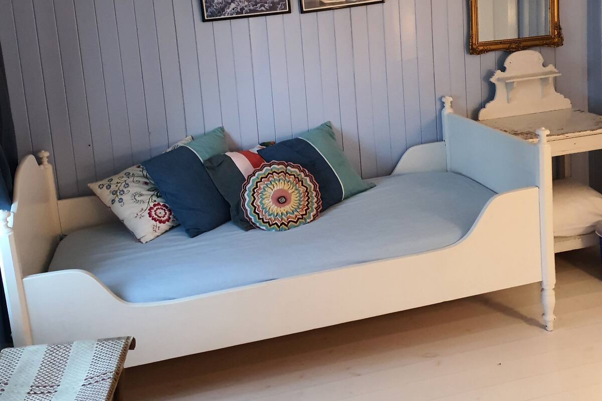 Una habitación con una cama blanca, una mesita y un espejo en la pared.