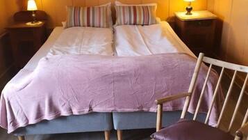 Une chambre à coucher comprenant un lit, deux tables de chevet, une chaise en bois et deux lampes fixées au mur.