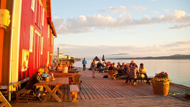 A wooden deck with tables and benches, overlooking a body of water and a distant shoreline. - Handelsstedet Forvik (Vevelstad)
