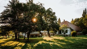 A house with a red roof, surrounded by a grassy yard and trees. - Kosbor Panzió (Magyarszombatfa)