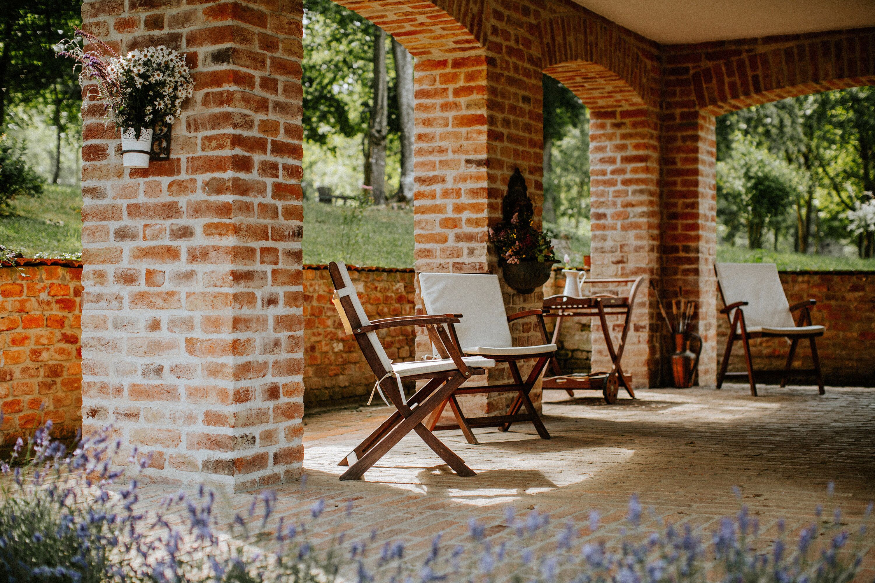 A covered patio area with brick walls, white cushioned chairs, and a table.