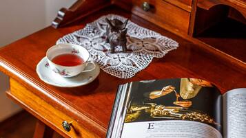 Un escritorio de madera con una taza de té, un posavasos de encaje y un libro abierto a una página que muestra una imagen de joyería.