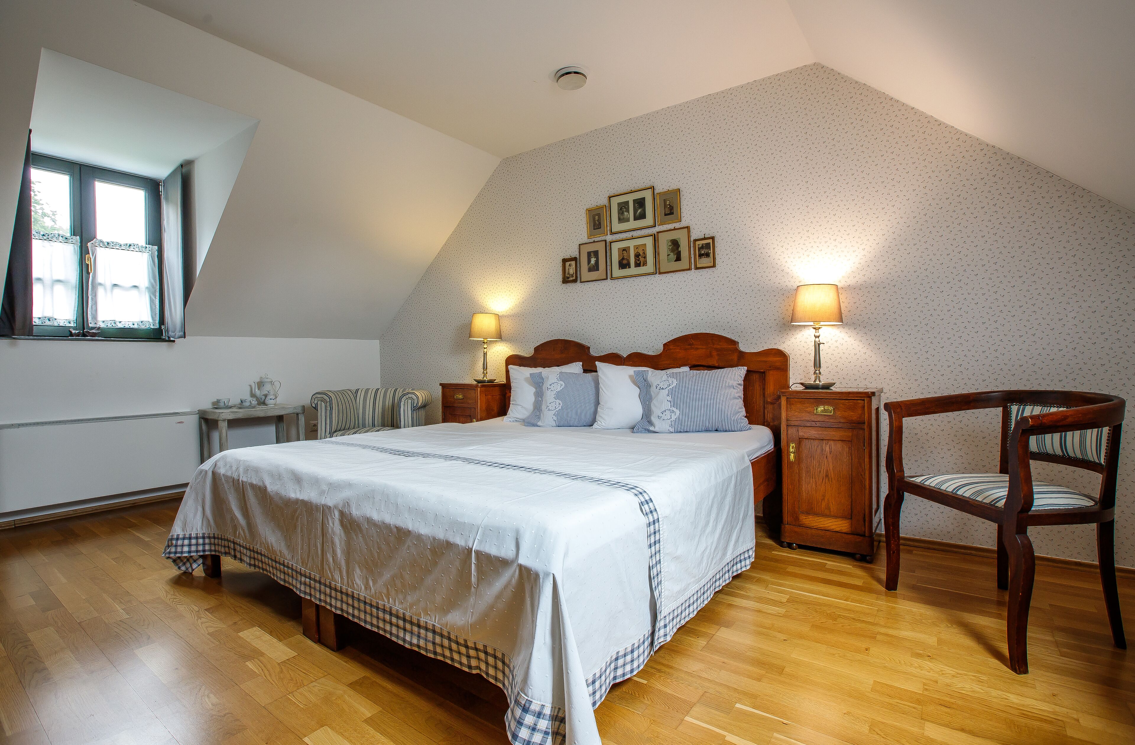 Een slaapkamer met een groot bed, twee nachtkastjes met lampen, een houten stoel en een raam met gordijnen.
