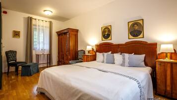 A hotel room with a large bed, two bedside tables with lamps, a wooden wardrobe, a chair, and a small table.