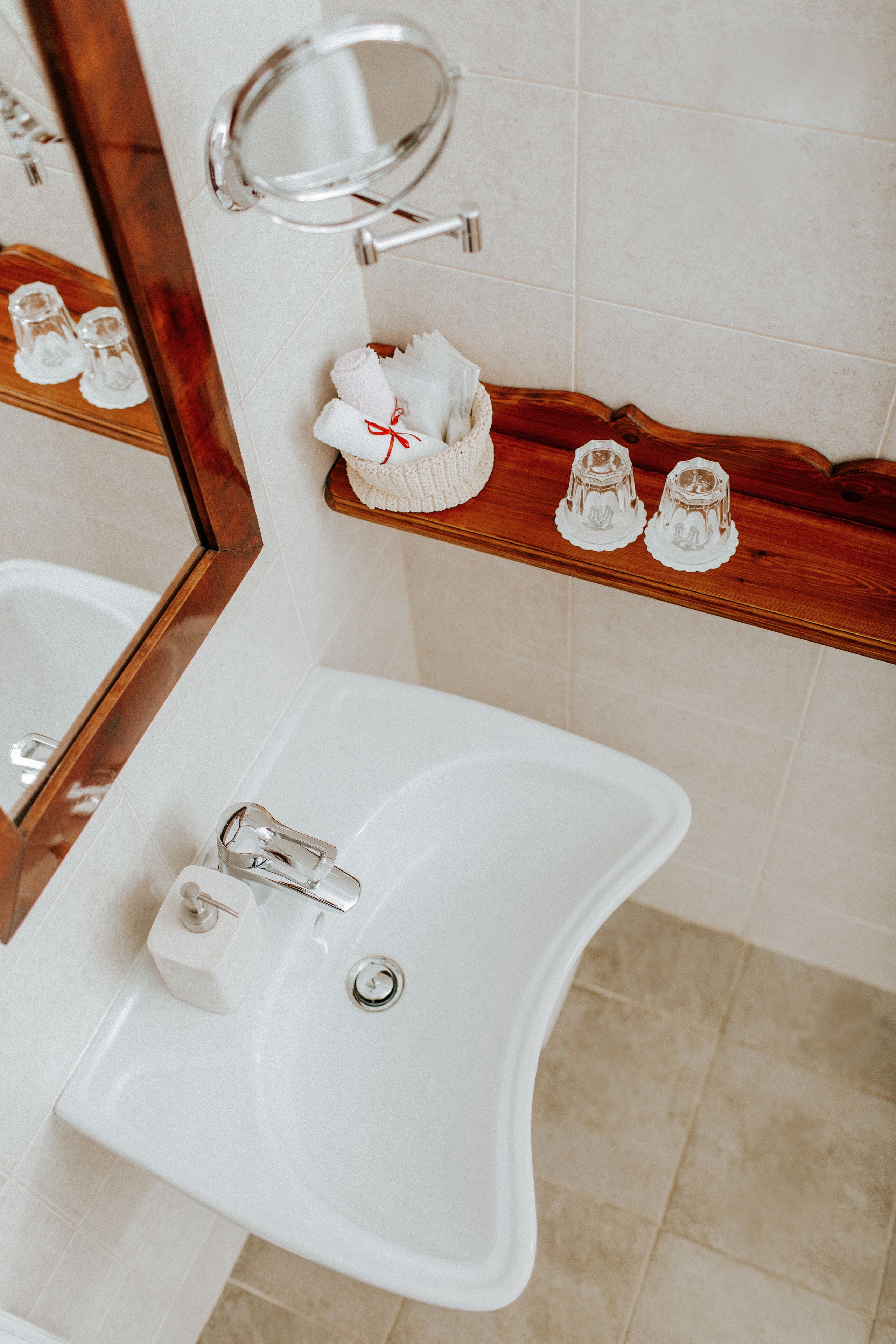 Un bagno con un lavandino bianco, uno scaffale in legno con articoli da toilette e uno specchio.
