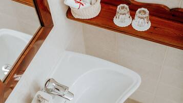 Un bagno con un lavandino bianco, uno scaffale in legno con articoli da toilette e uno specchio.