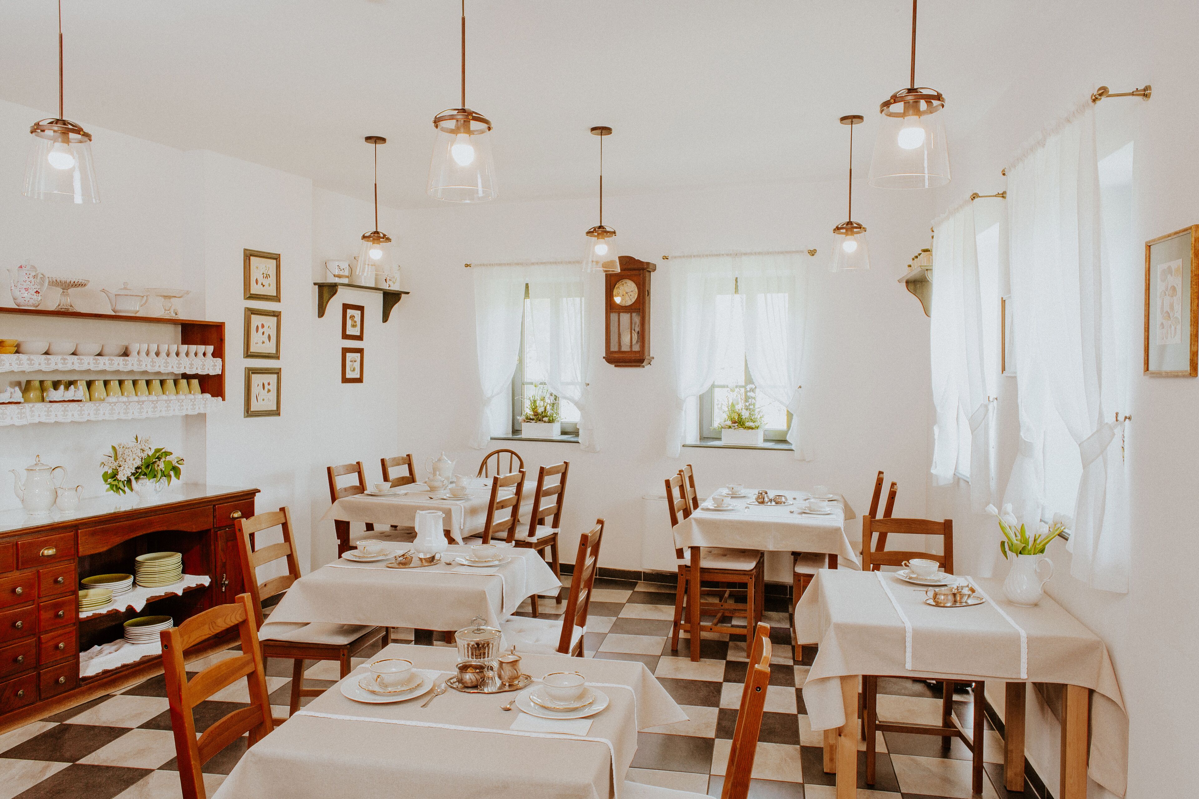 A dining area with multiple tables and chairs, wooden cabinets, and hanging light fixtures.