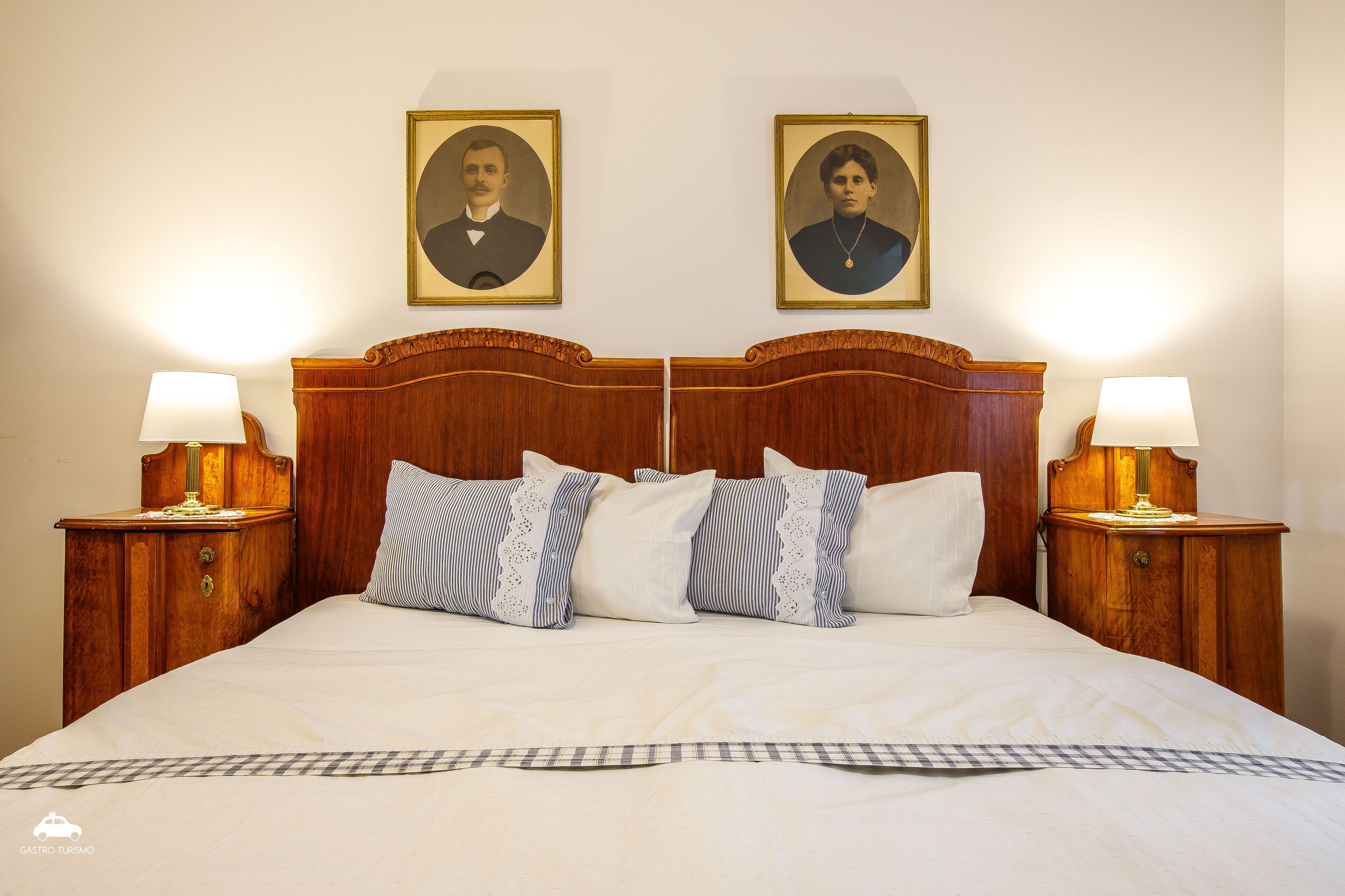 A hotel room with a large bed, two bedside tables with lamps, and two framed portraits on the wall.