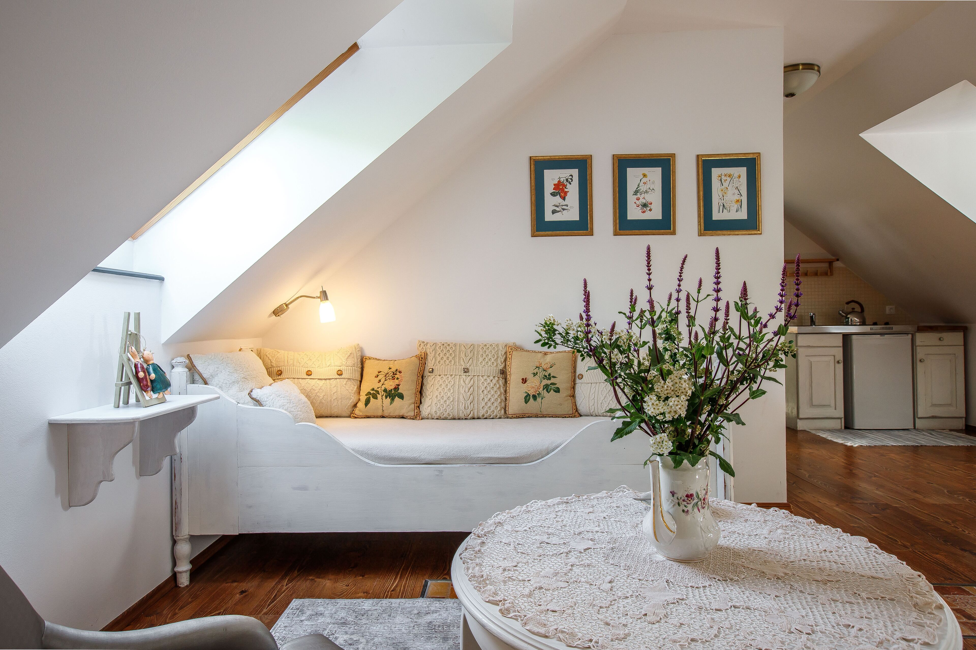 A cozy loft bedroom with a sloped ceiling, a white bed, a bedside table, and a vase of flowers.